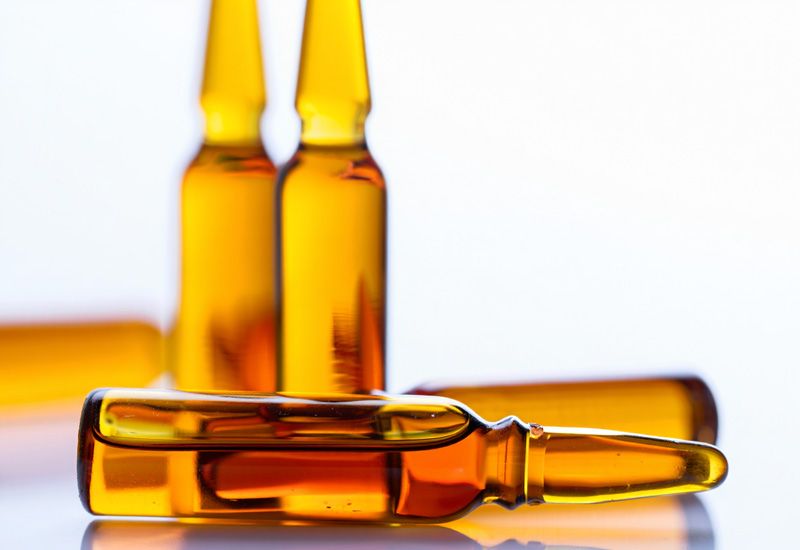 Пять оранжевых ампул лежат на белом столе под ярким освещением